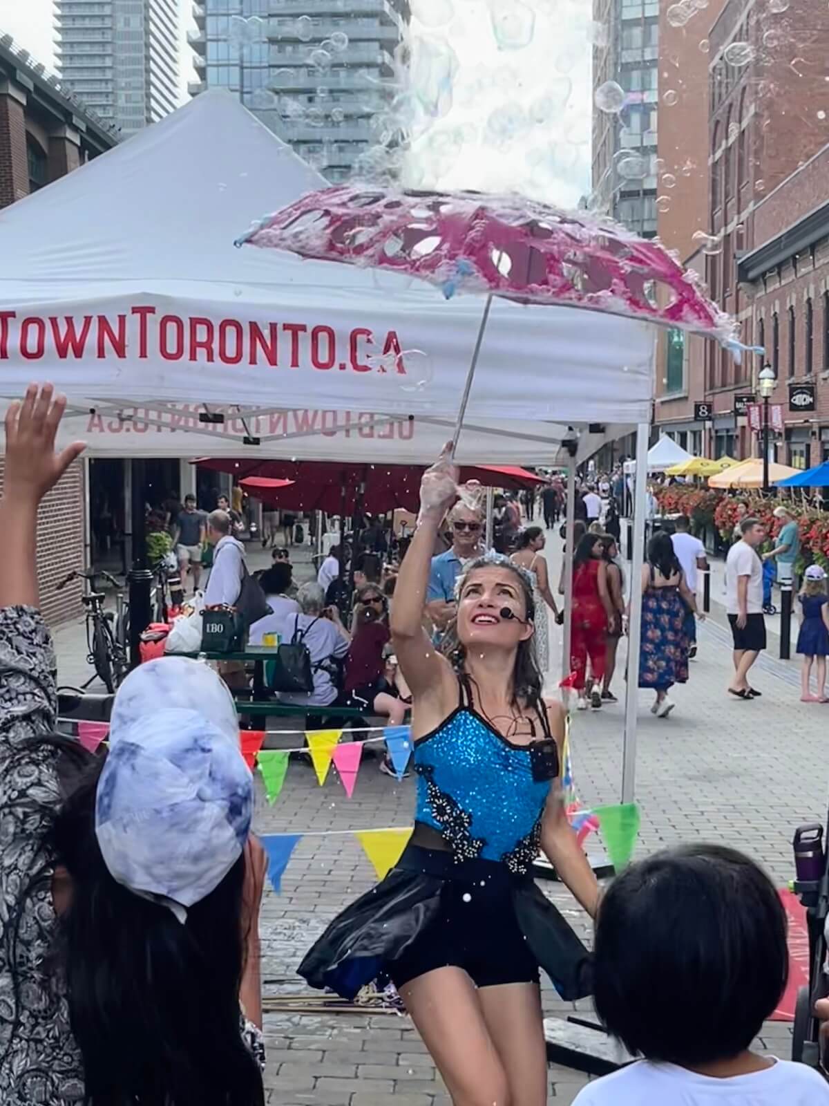 A woman in a blue and black dress is holding up a pink umbrella while bubbles rain down